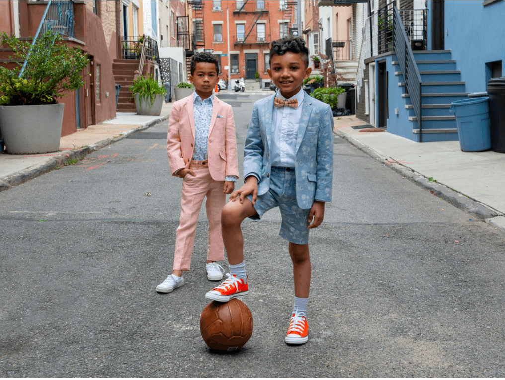 Two stylish boys in playful suits enjoying a fun day outside with a basketball, showcasing modern kids' fashion.