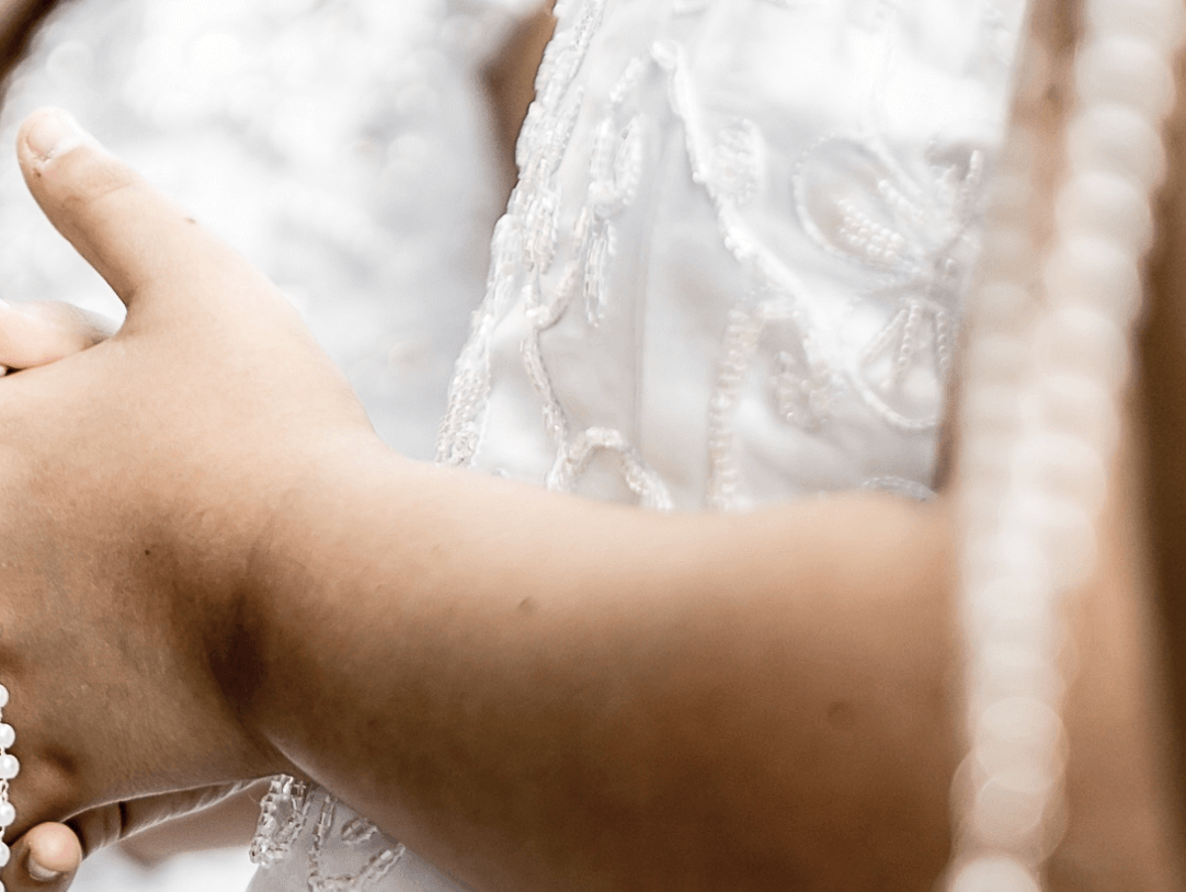 Close-up of a young girl’s hands holding a rosary, showcasing elegance for a First Communion outfit.