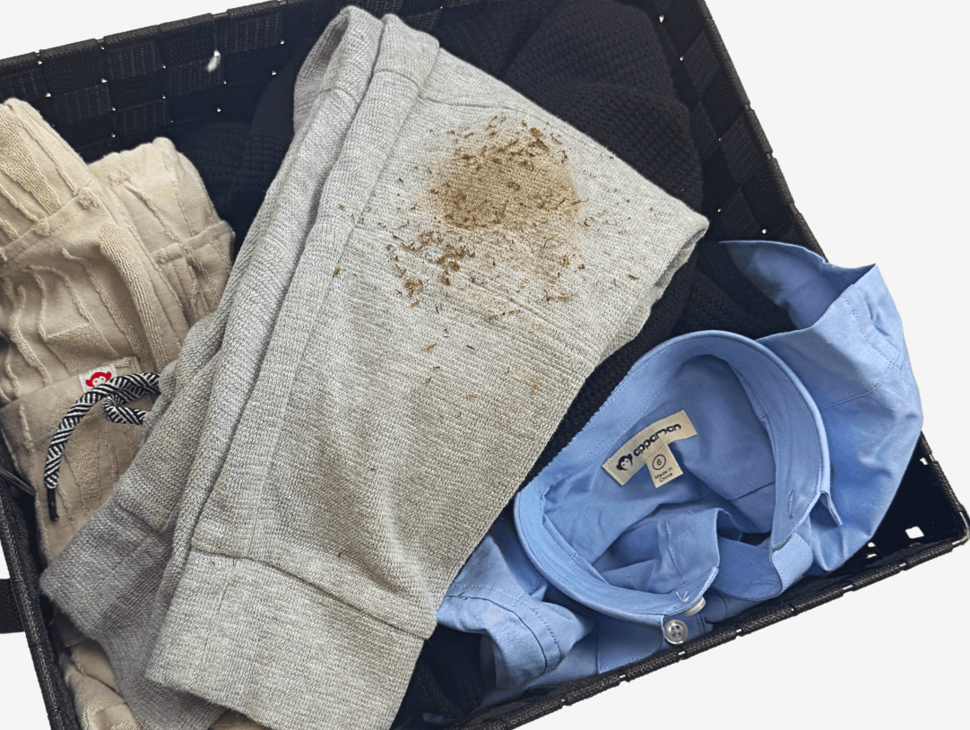A laundry basket filled with kids' clothes showing dirt stains, highlighting the playful adventures of childhood.