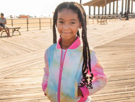 Stylish girl smiling in a vibrant tie-dye jacket, showcasing fun kids fashion for parents' style guides.