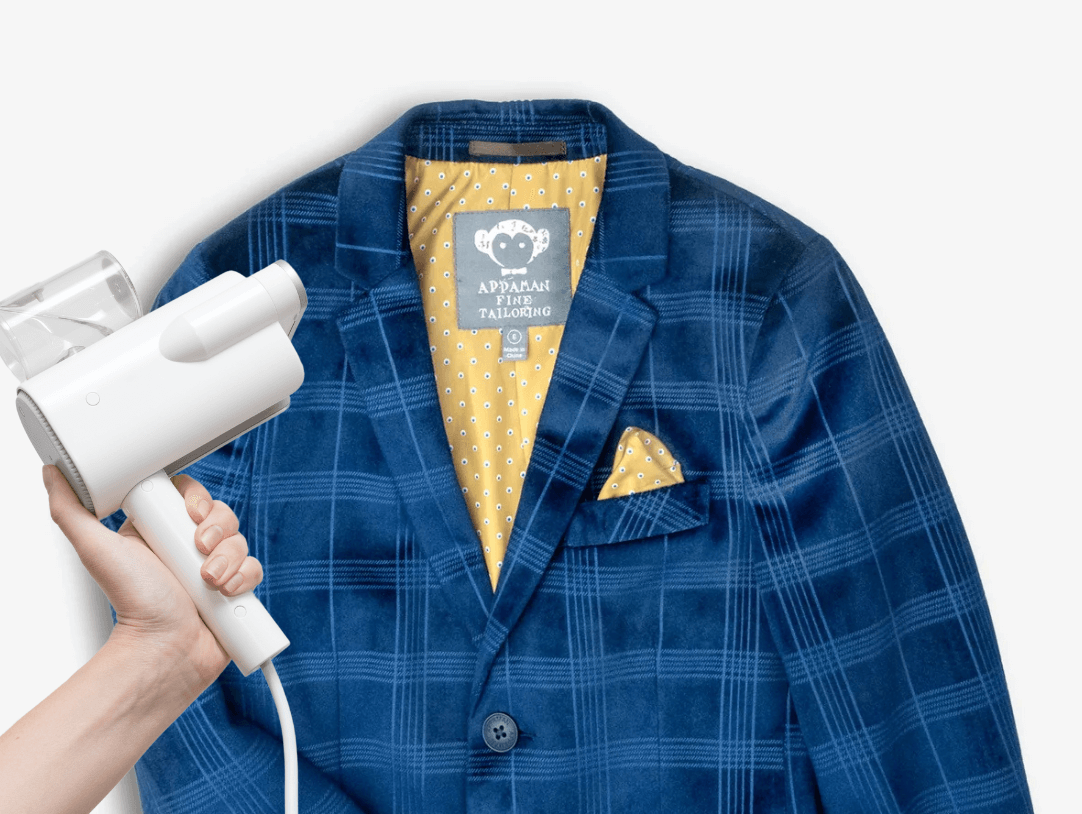 Hand holding a steamer over a stylish blue suit jacket, perfect for parents looking to freshen up kids' outfits.