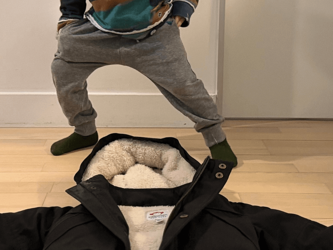 Toddler playfully refusing to wear a stylish winter coat, showcasing parent challenges in kids' winter styling.