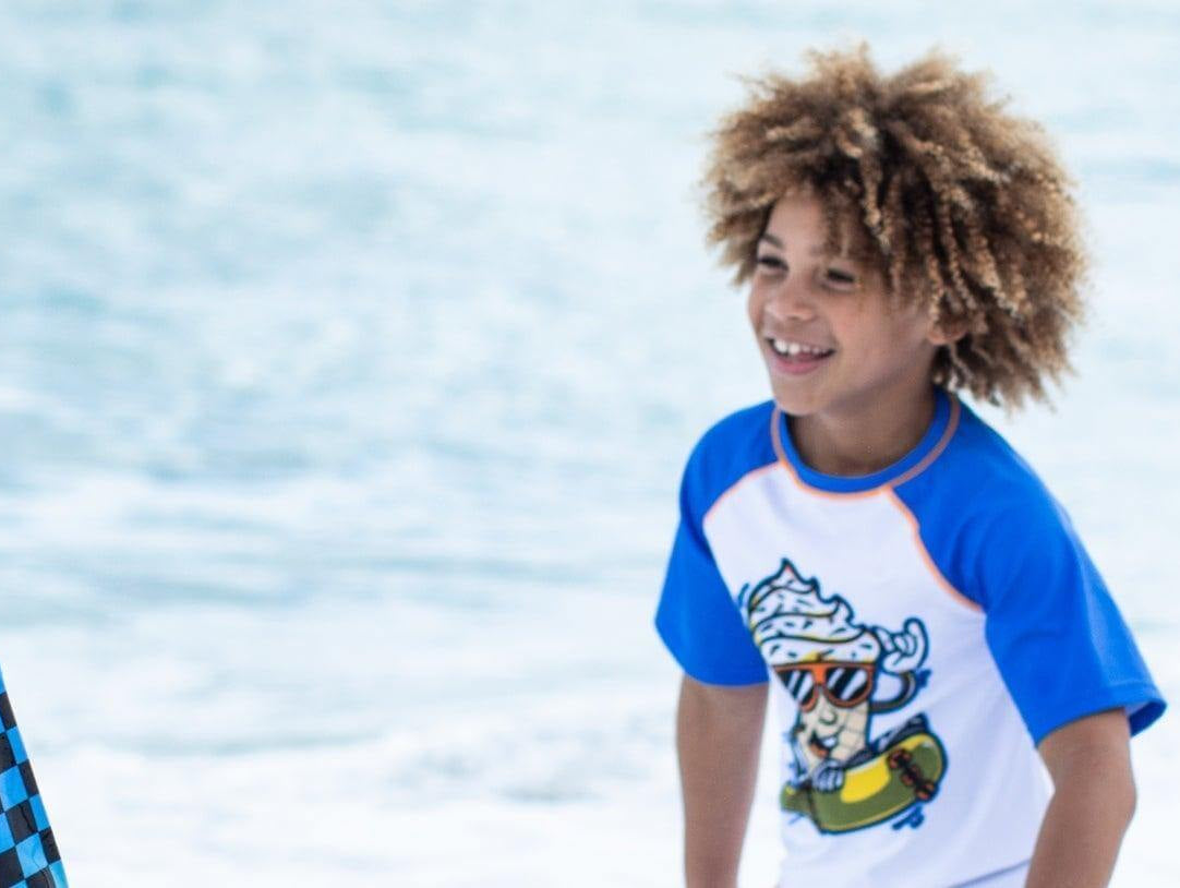 Three stylish kids in vibrant swim shirts enjoying a sunny day at the beach, embodying fun and safety in sun protection.