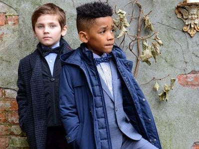 Two stylish boys showcase modern outerwear and tailored looks, perfect for kids’ fashion and striking a confident pose.