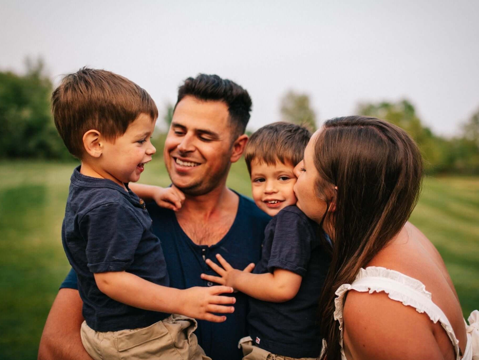Joyful family moment with two boys in stylish outfits, captured in a lush outdoor setting.