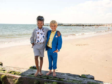 Two stylish kids in vibrant suits enjoying a beach day, showcasing playful summer suiting options for boys.