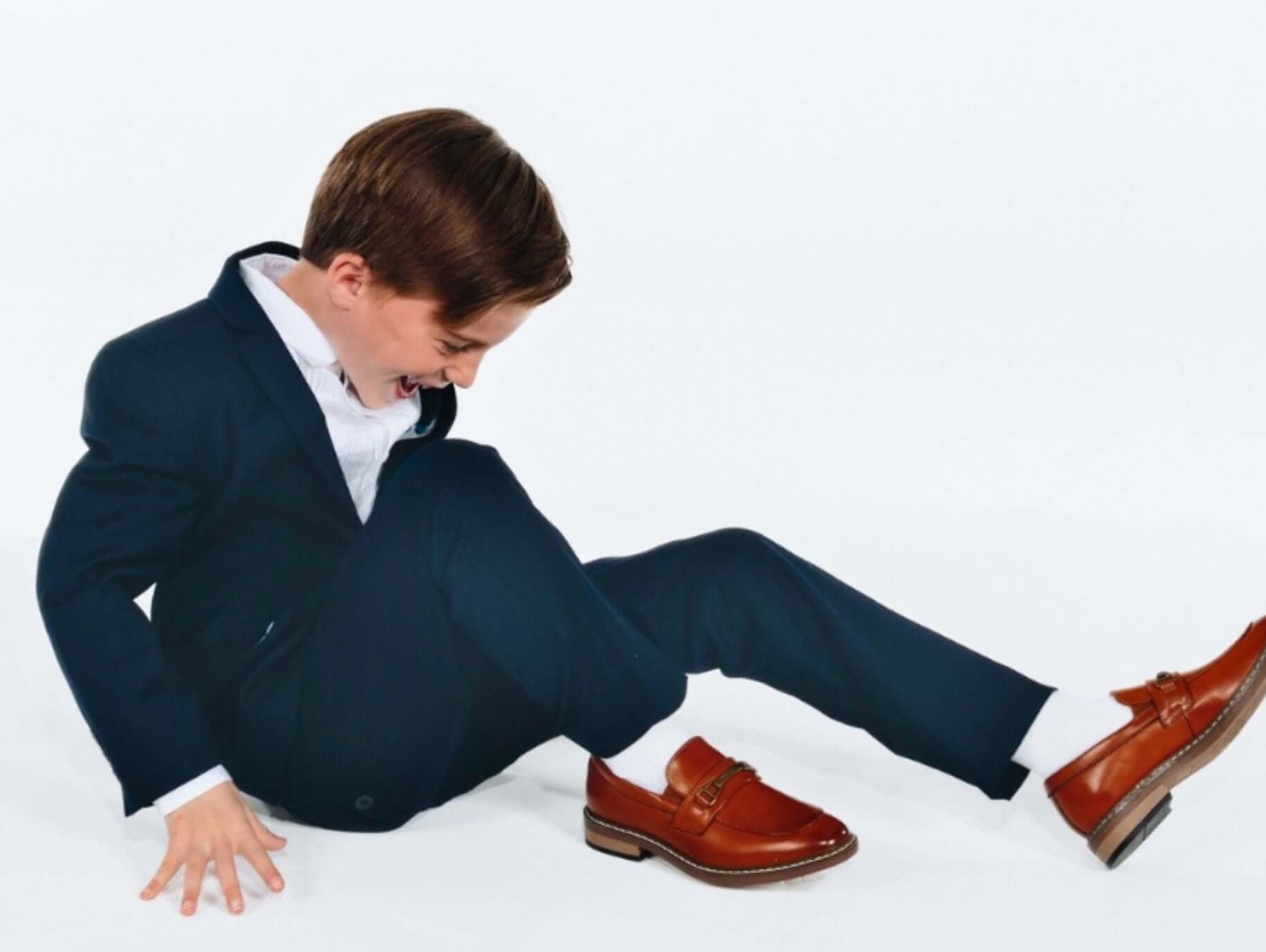 Stylish young boy in a tailored suit and smart shoes, showcasing playful Bar Mitzvah attire for modern kids.