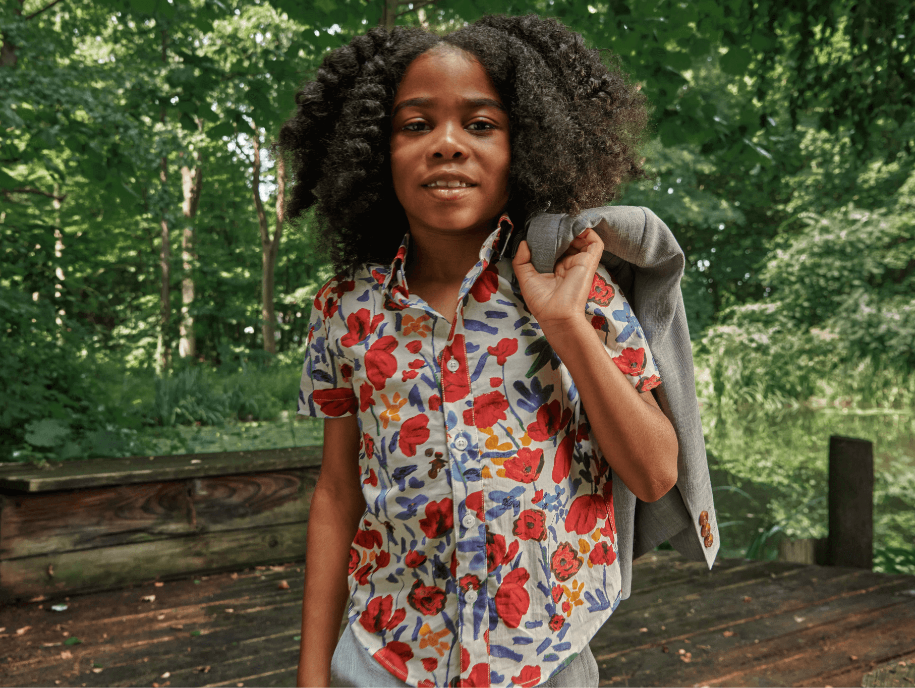 Stylish child in a vibrant floral shirt holding a blazer, showcasing playful eco-friendly fashion for kids.