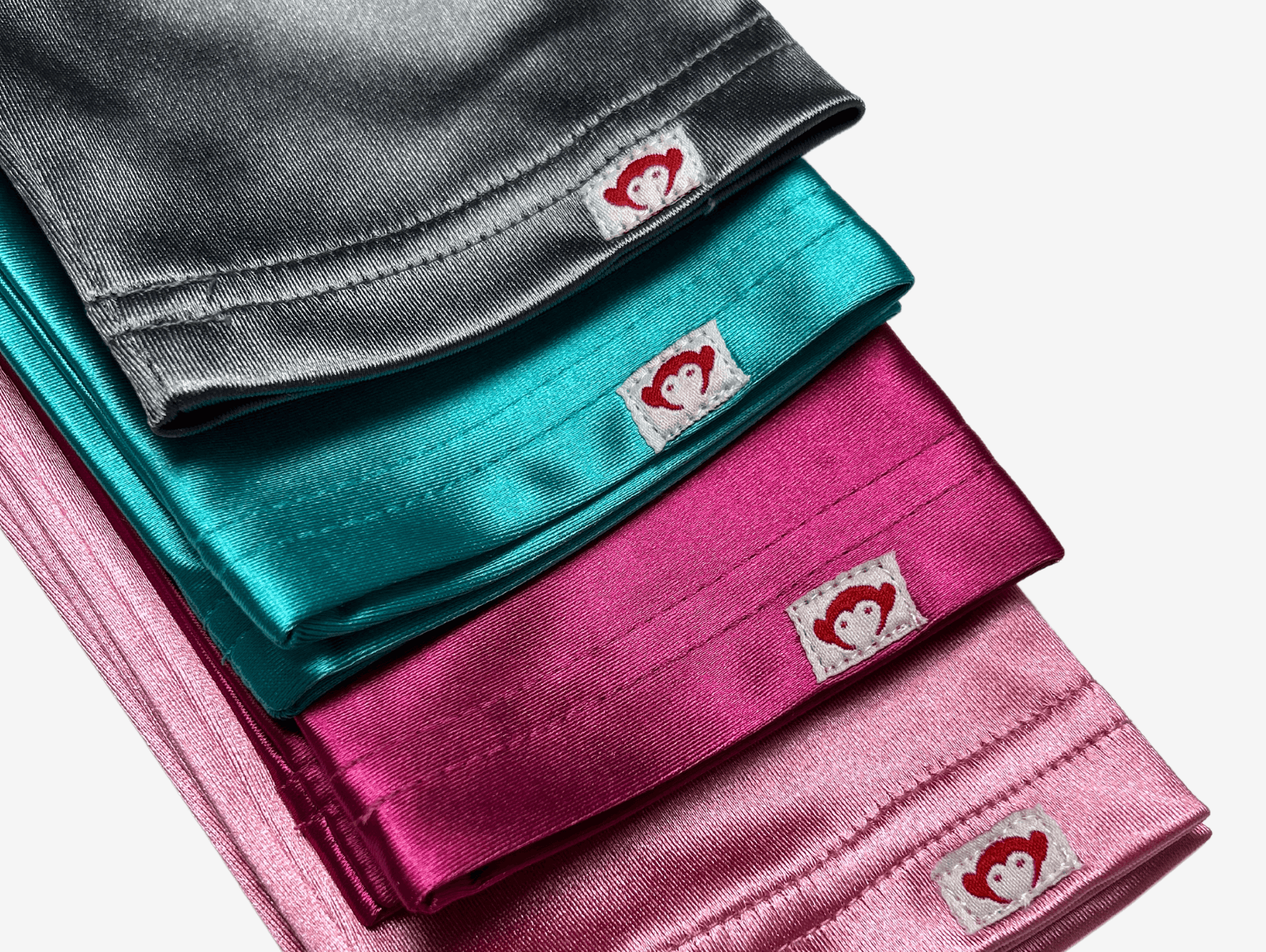 Colorful satin sleepover pillowcases in shades of grey, teal, pink, and fuchsia, featuring a playful heart logo.