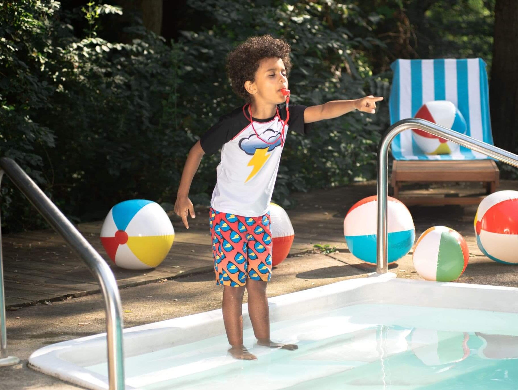 Stylish kid playfully ready to dive into the pool, wearing cool beach shorts and a playful tee, surrounded by colorful beach balls.