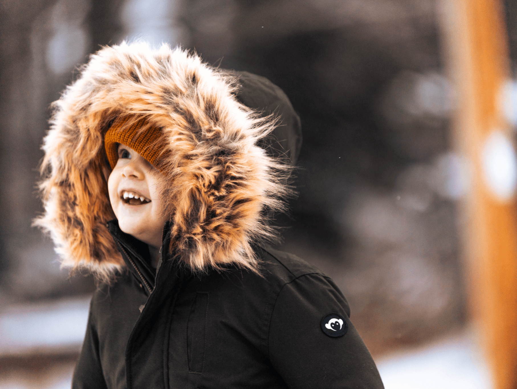 Stylish toddler in a cozy winter parka with a fur-lined hood, enjoying the snowy outdoors with a bright smile.
