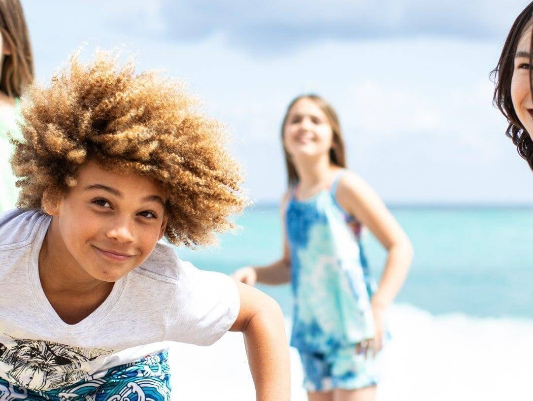 Four joyful kids playing on the beach in vibrant Appaman swimwear, ready for summer fun and adventure.
