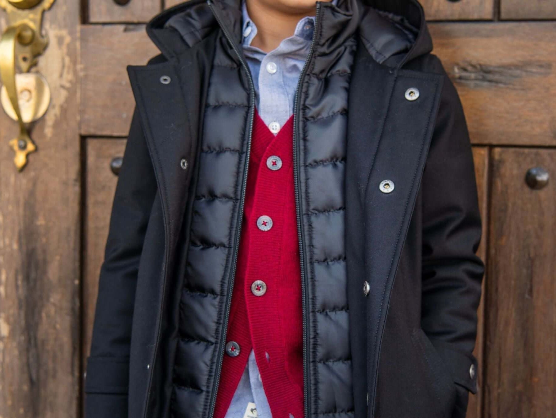 Stylish boy in a cozy black parka layered over a red vest, showcasing trendy winter formal fashion.