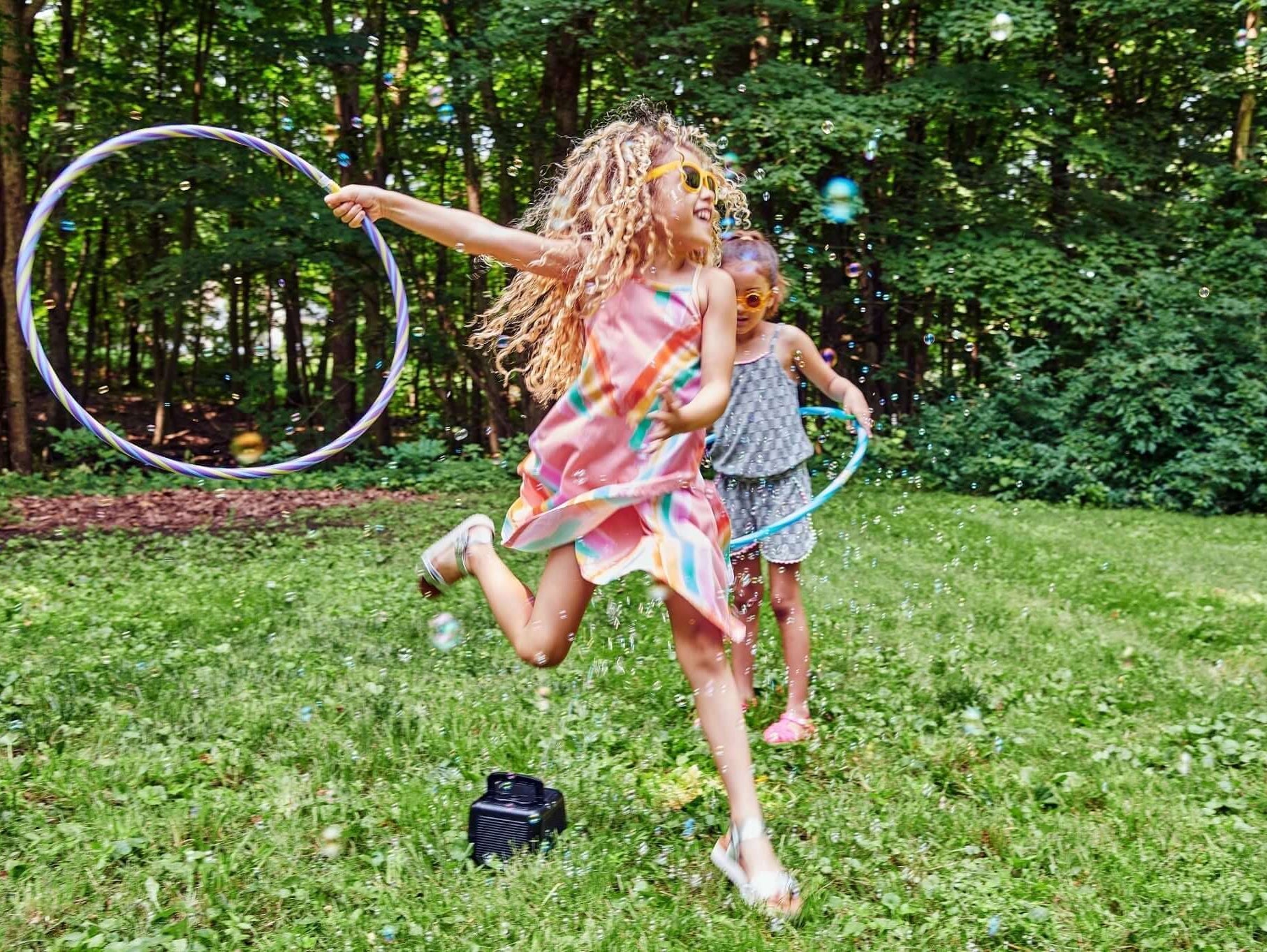 Two joyful girls playing with hula hoops in a vibrant green backyard, celebrating spring in stylish outfits.