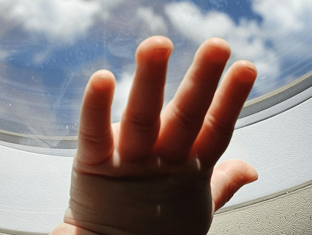 Toddler's hand reaching out to airplane window, enjoying sky views during travel adventures.