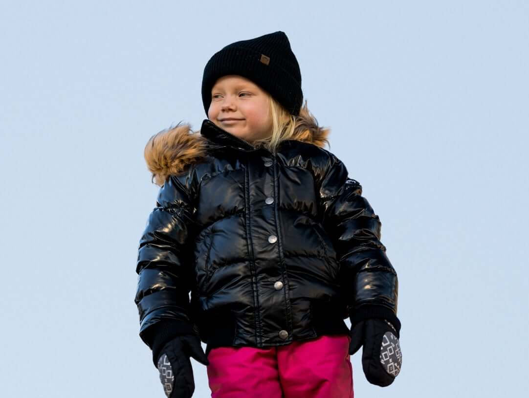 Confident child in a stylish black puffer coat and pink pants, ready for winter adventures in the snow.