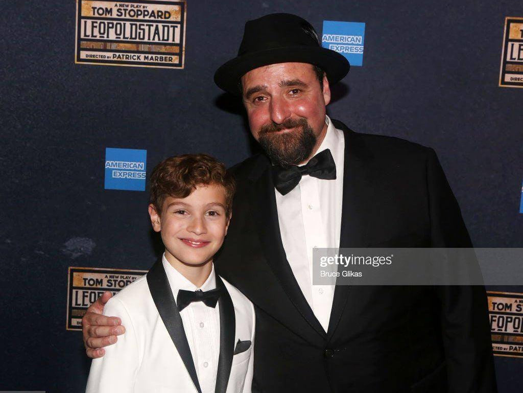 Stylish duo at Leopoldstadt opening: a boy in a white tux and a man in black suit, showcasing kids' suit styling tips.