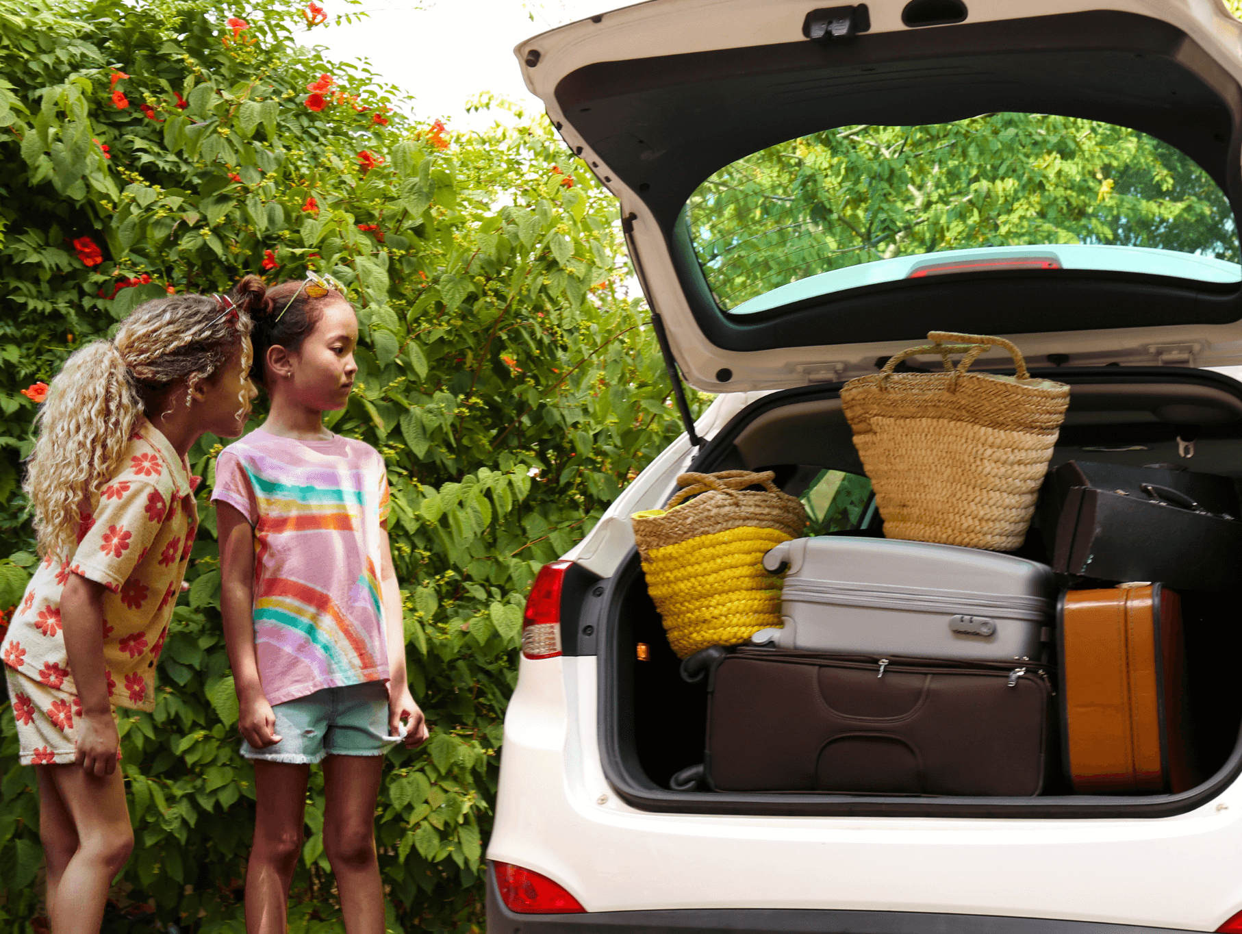 Two girls excitedly peeking into a packed car with vibrant luggage, ready for a fun road trip adventure.