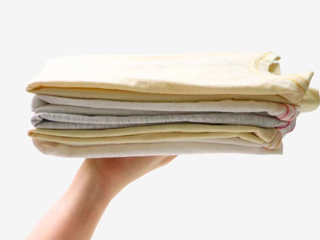 A hand holding a neatly stacked pile of kids' clothes in soft pastel colors, showcasing organized laundry tips.