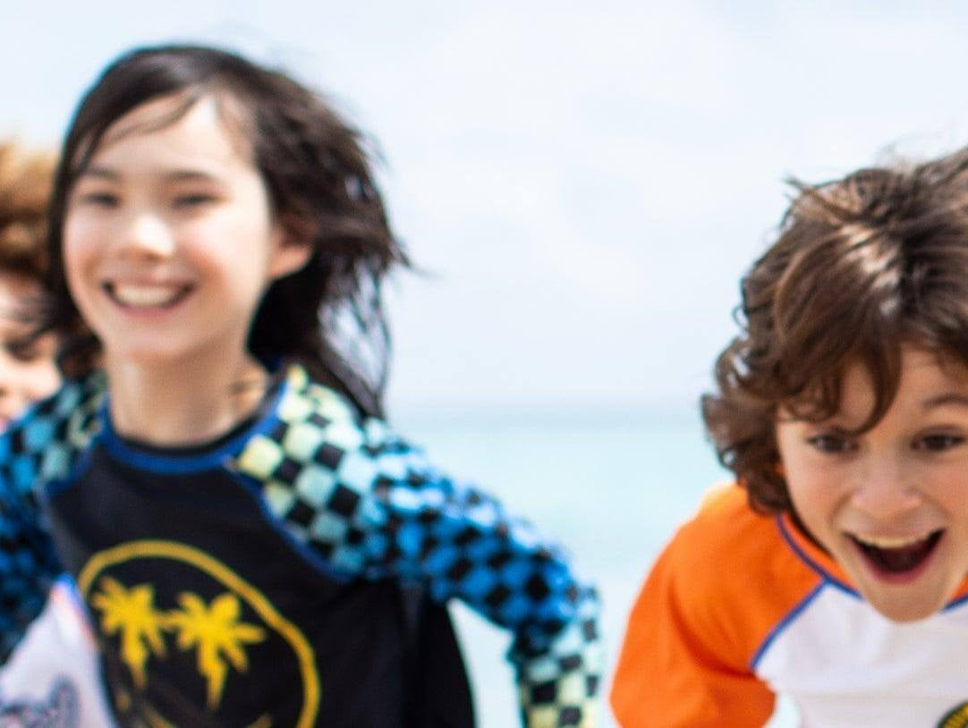 Kids joyfully playing on the beach in vibrant UPF 50 swimwear, showcasing style and sun safety.