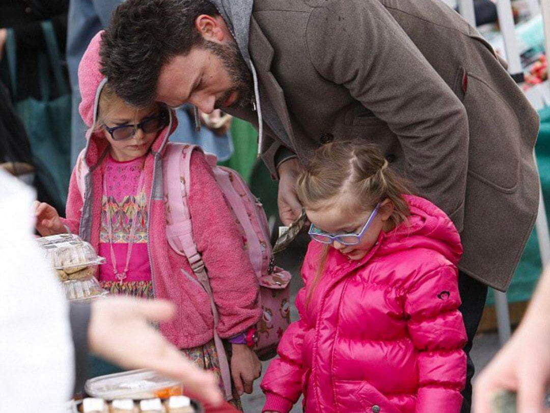 Ben Affleck interacts with daughters at a market, showcasing stylish kids' winter wear, including Violet's vibrant pink Appaman coat.