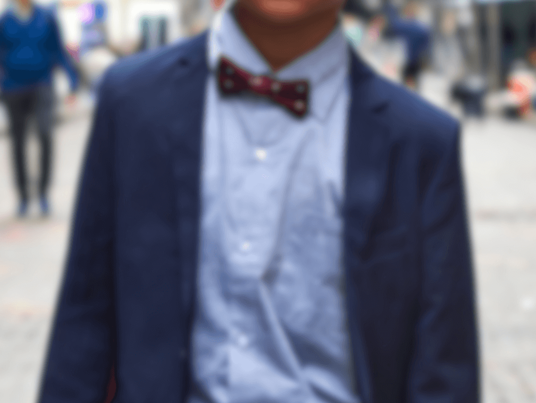A stylish young boy in a suit and bow tie confidently enjoys urban life, showcasing contemporary kids fashion.
