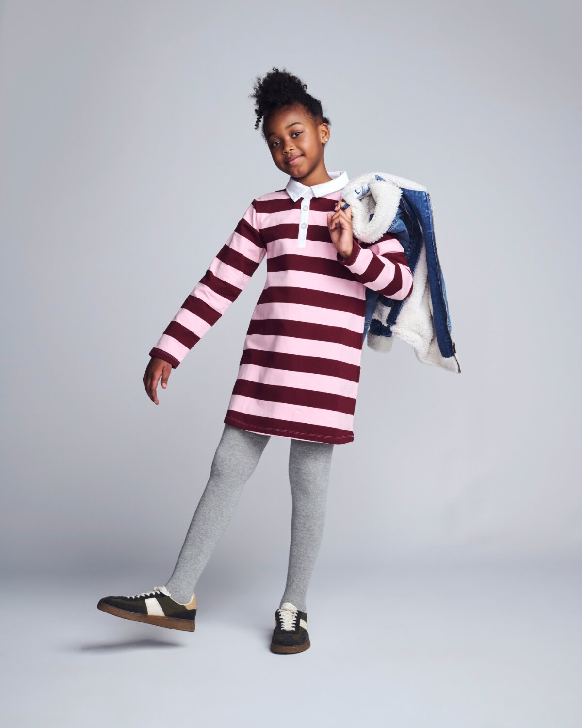 Child wearing a red and white striped dress holding a jacket against a gray background