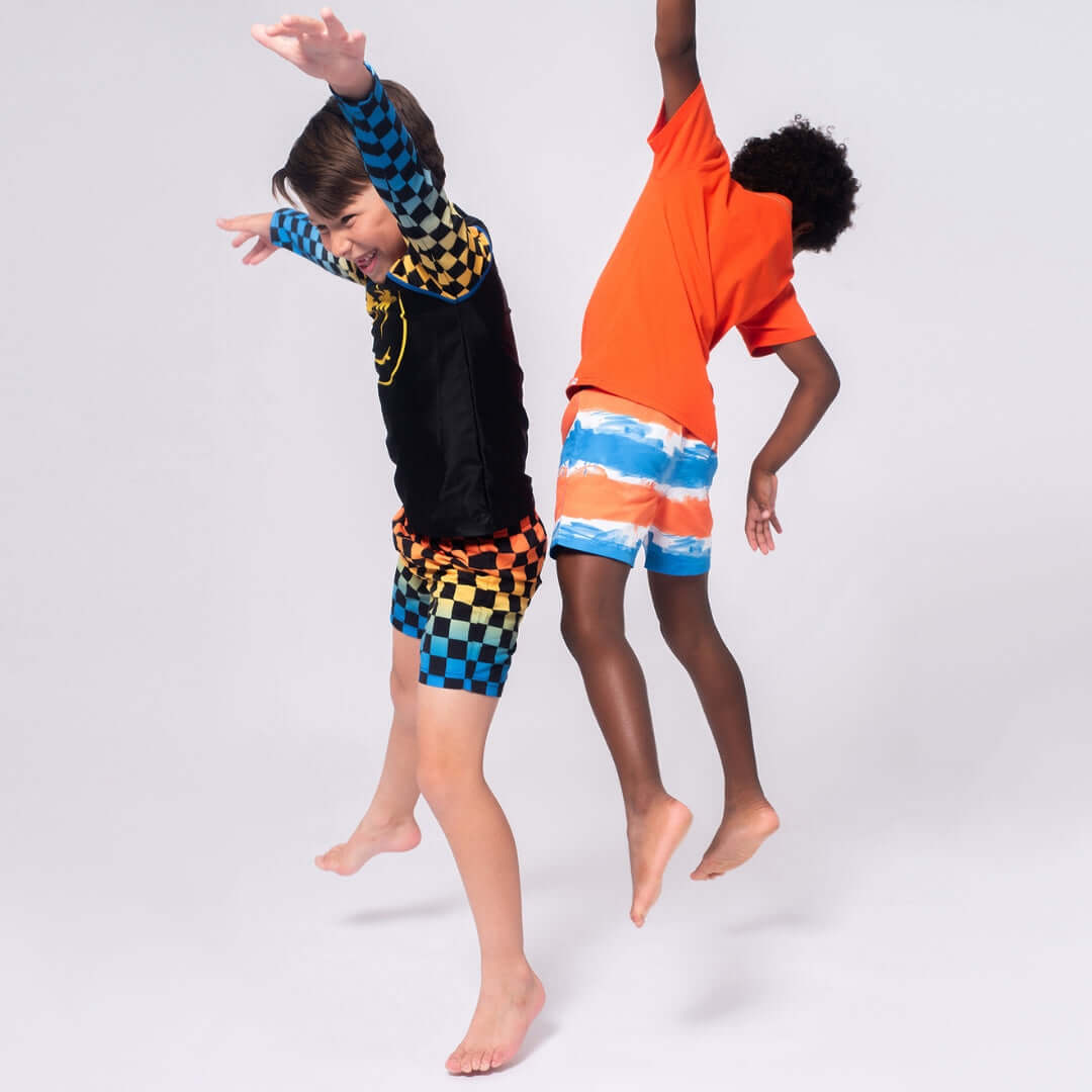 Two kids joyfully jumping in stylish swimwear—colorful checks and fun stripes—ready for summer adventures!