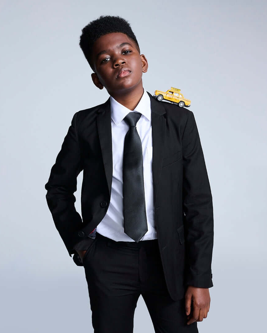 Boys' Black Suits collection featuring a stylish boy in a black suit with a playful toy car on his shoulder.