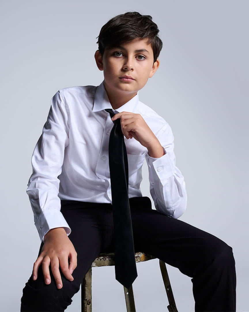 Boys' White Button Down Shirts worn by a confident boy sitting with a black tie, showcasing modern style.