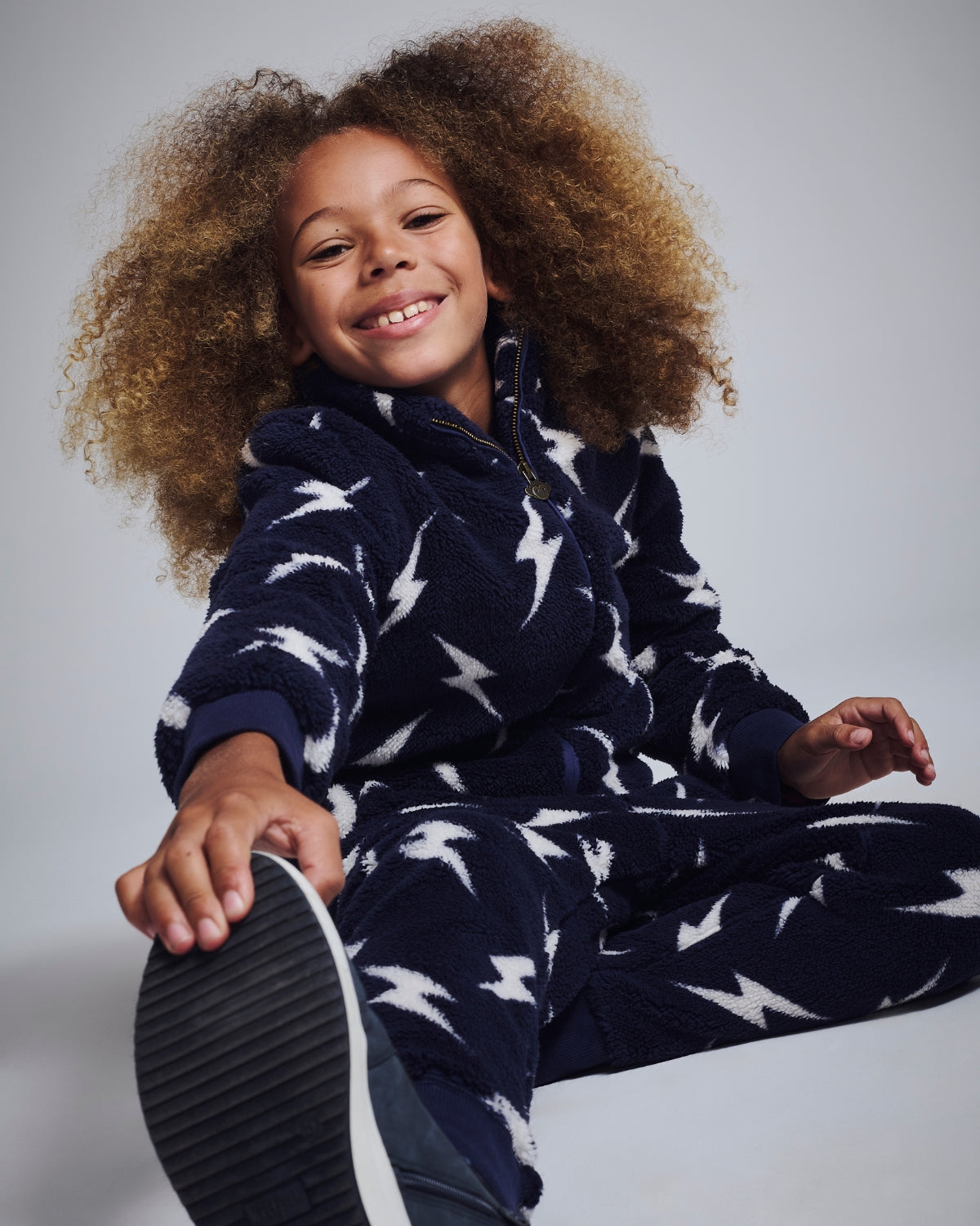 Excited girl surrounded by sparkly confetti, unwrapping a festive gift from Appaman's stylish collection.