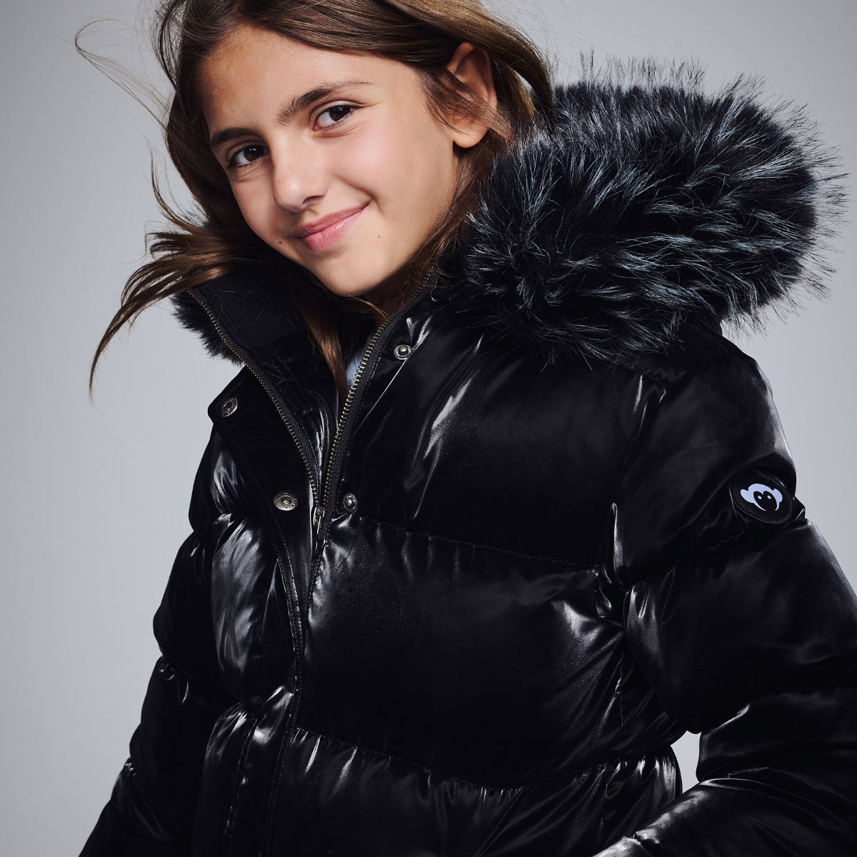 Kids’ Jackets & Coats featuring a girl smiling in a black puffer jacket with a fur-lined hood.
