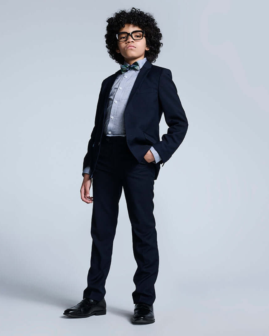 Stylish boy in navy suit from the Boys' Core Suiting collection with a bow tie and glasses.