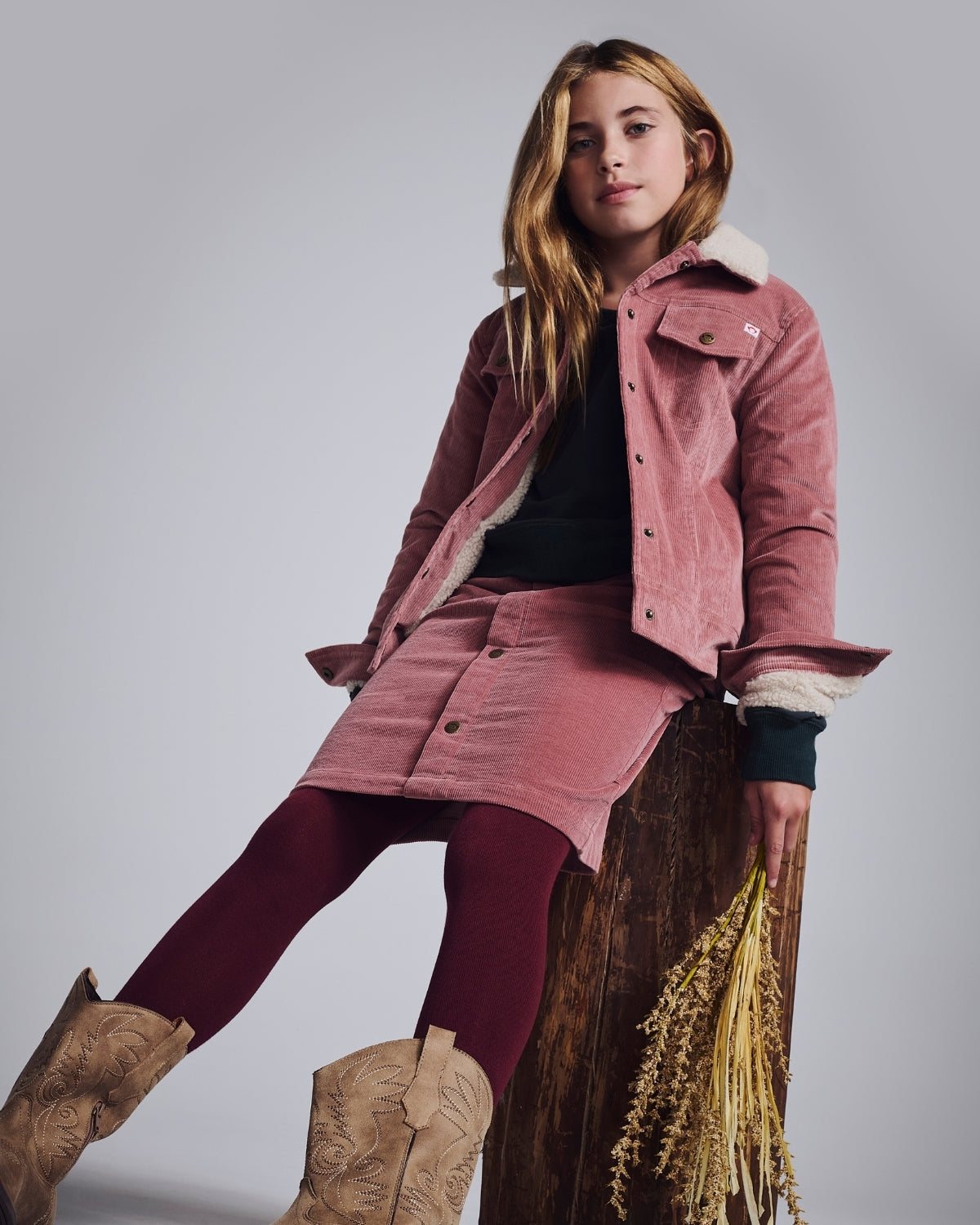 A girl in a pink shirt playfully makes a heart with her hands, showcasing trendy girls' summer fashion.