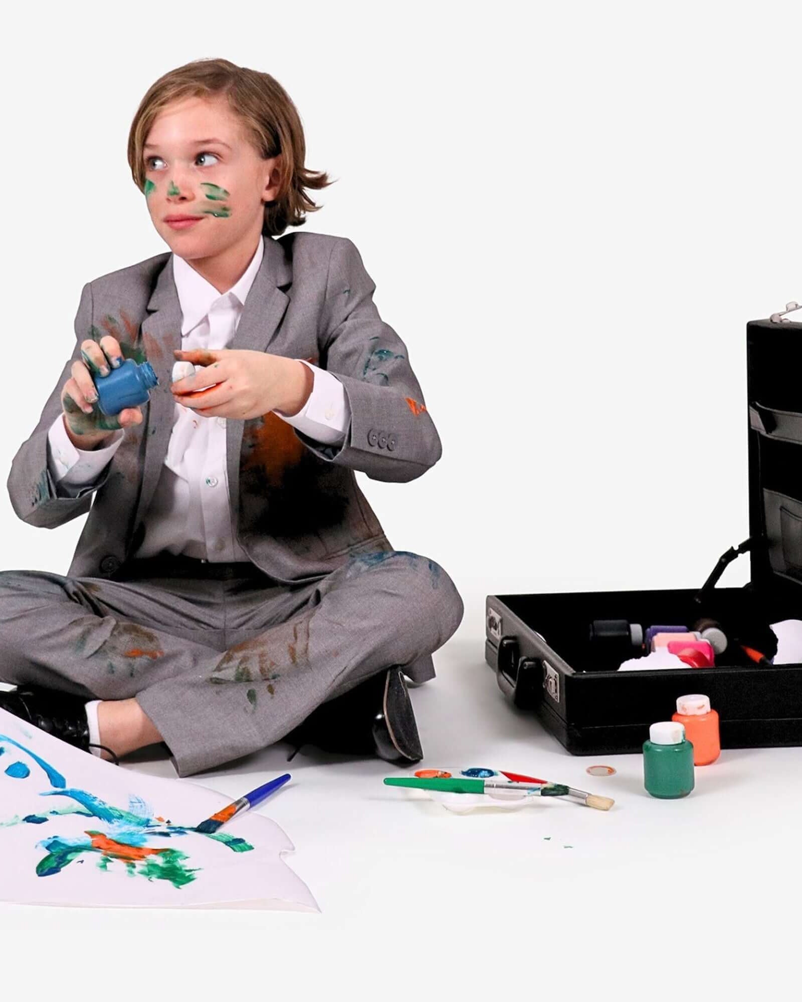 Boy in Boys' Machine Washable Suiting covered in paint, creating art with a mess of colors around him.