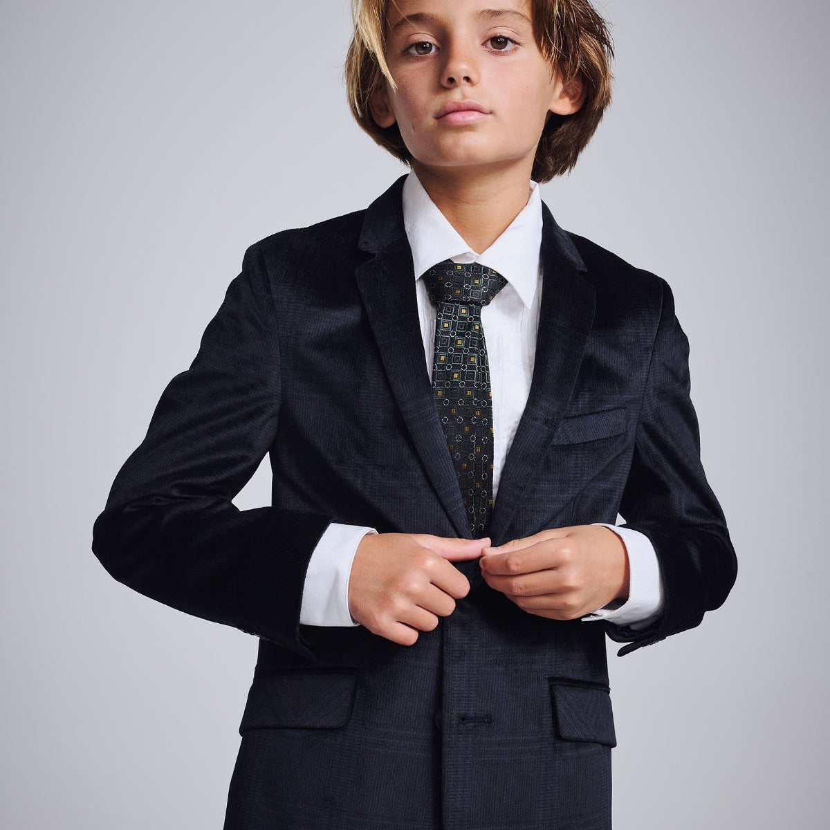 Stylish boy in a sharp black suit and tie, playfully strutting with a briefcase—making formal wear fun!