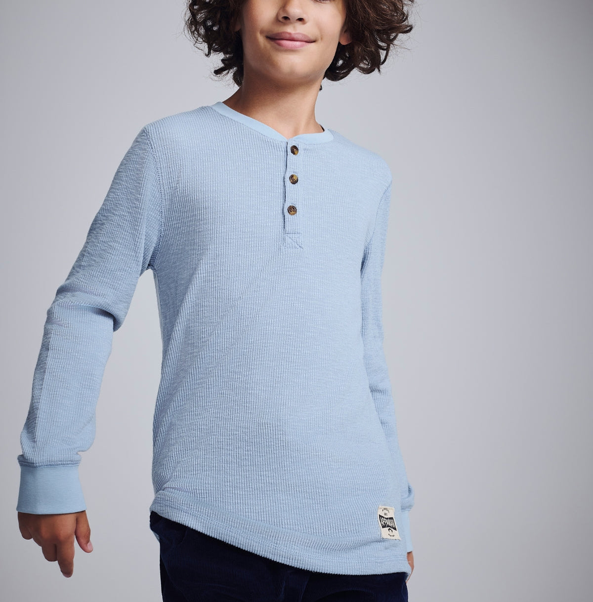 Stylish boy in a palm-print Henley shirt holding a vintage soccer ball, radiating fun and adventure.