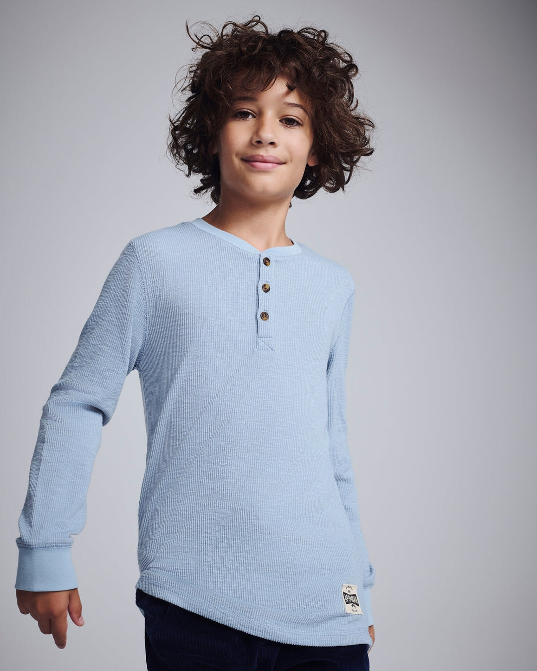 Stylish boy in a palm-print Henley shirt holding a vintage soccer ball, radiating fun and adventure.