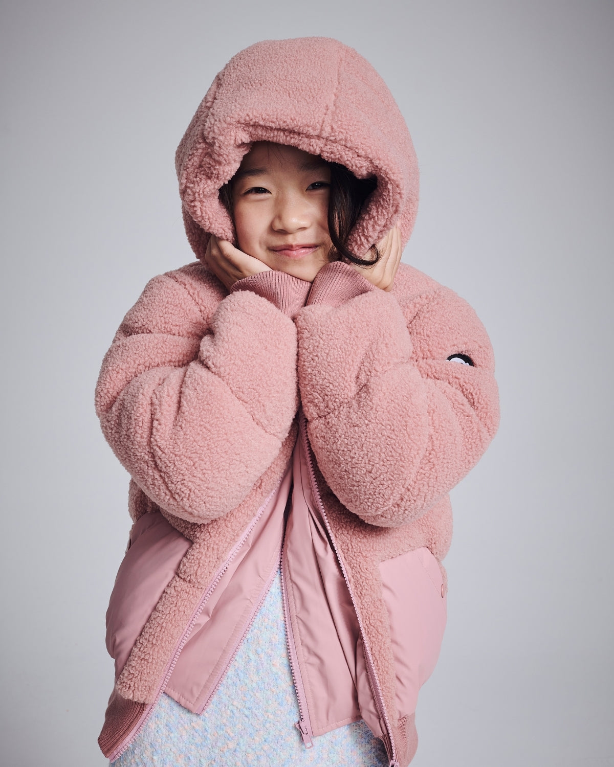 Best Selling Kids’ Clothing: Cozy pink outerwear for kids, featuring a fluffy hood and a cheerful expression.