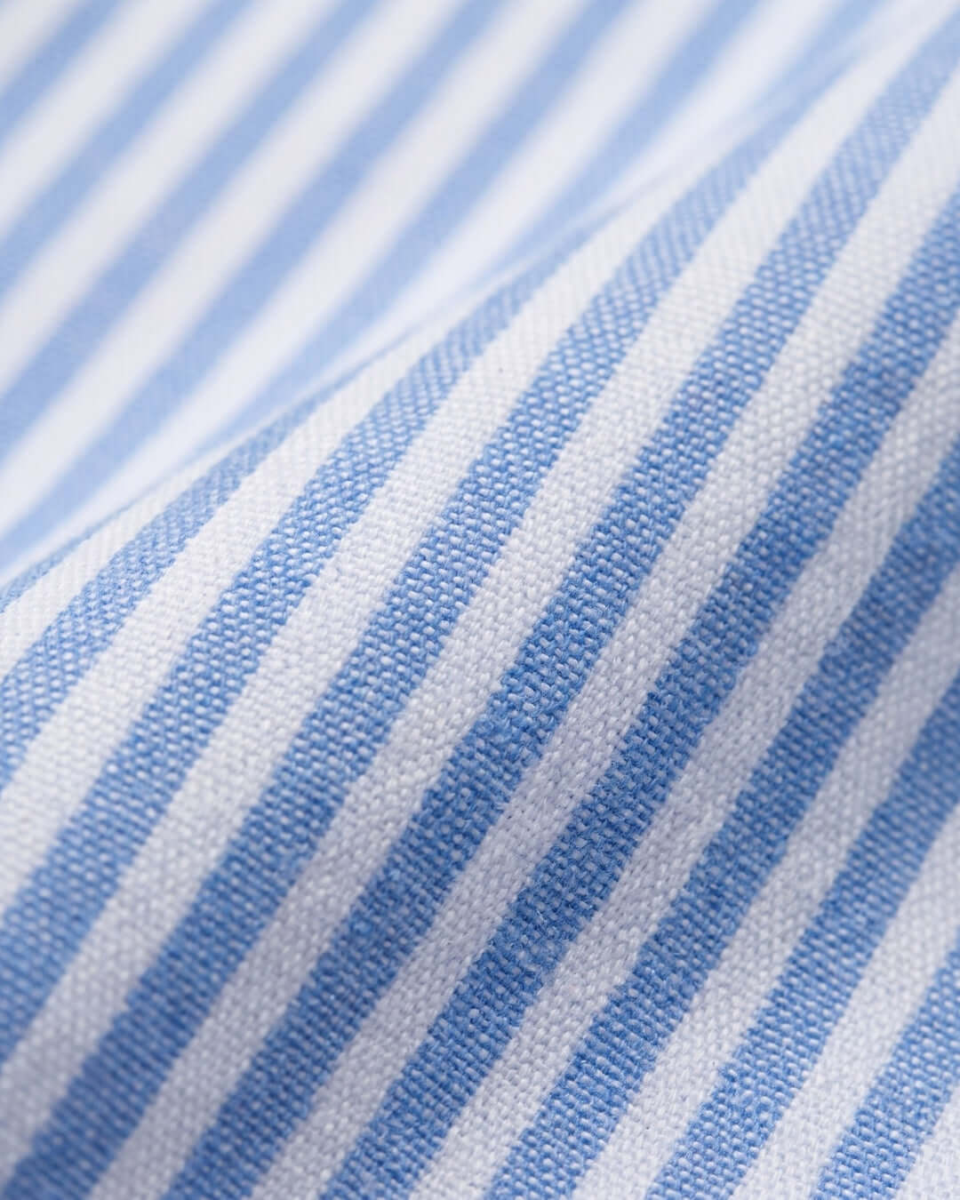 A close-up of a blue and white striped fabric with a visible woven texture and soft folds.