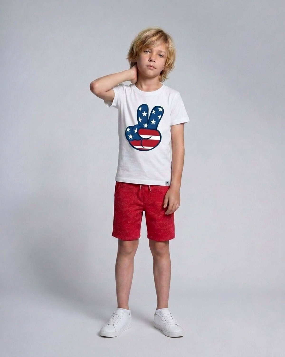 Child wearing a white t-shirt with a colorful graphic and red shorts on a gray background