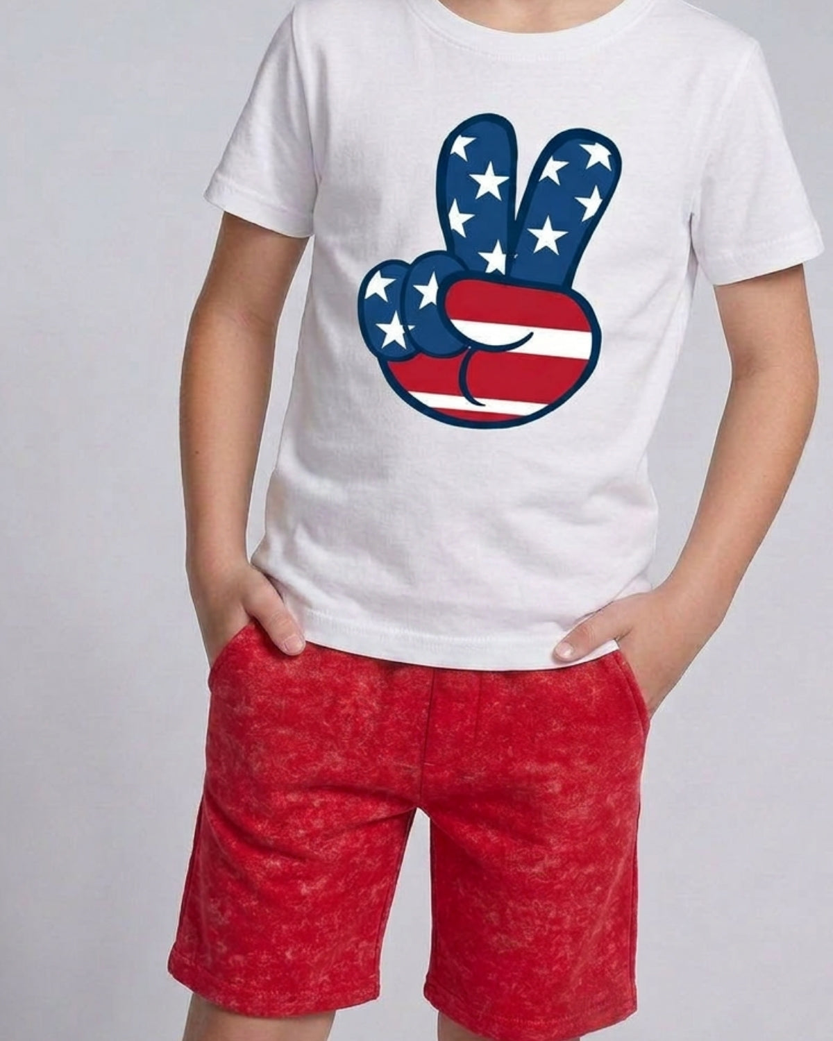 Person wearing a white t-shirt with a peace sign design featuring the American flag, paired with red shorts on a light gray background.