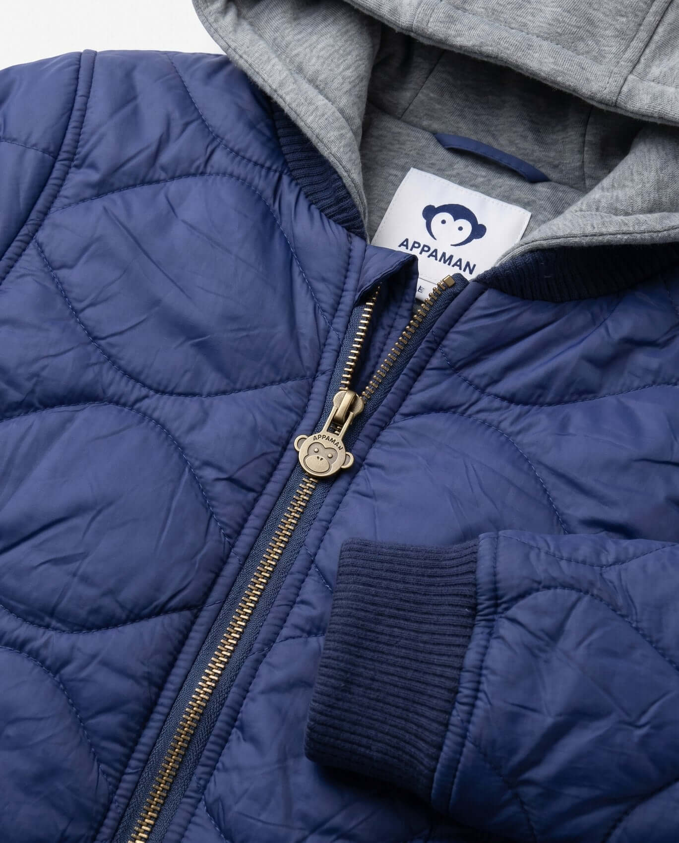 Close-up of a blue quilted jacket with a gray hood and Appaman label.