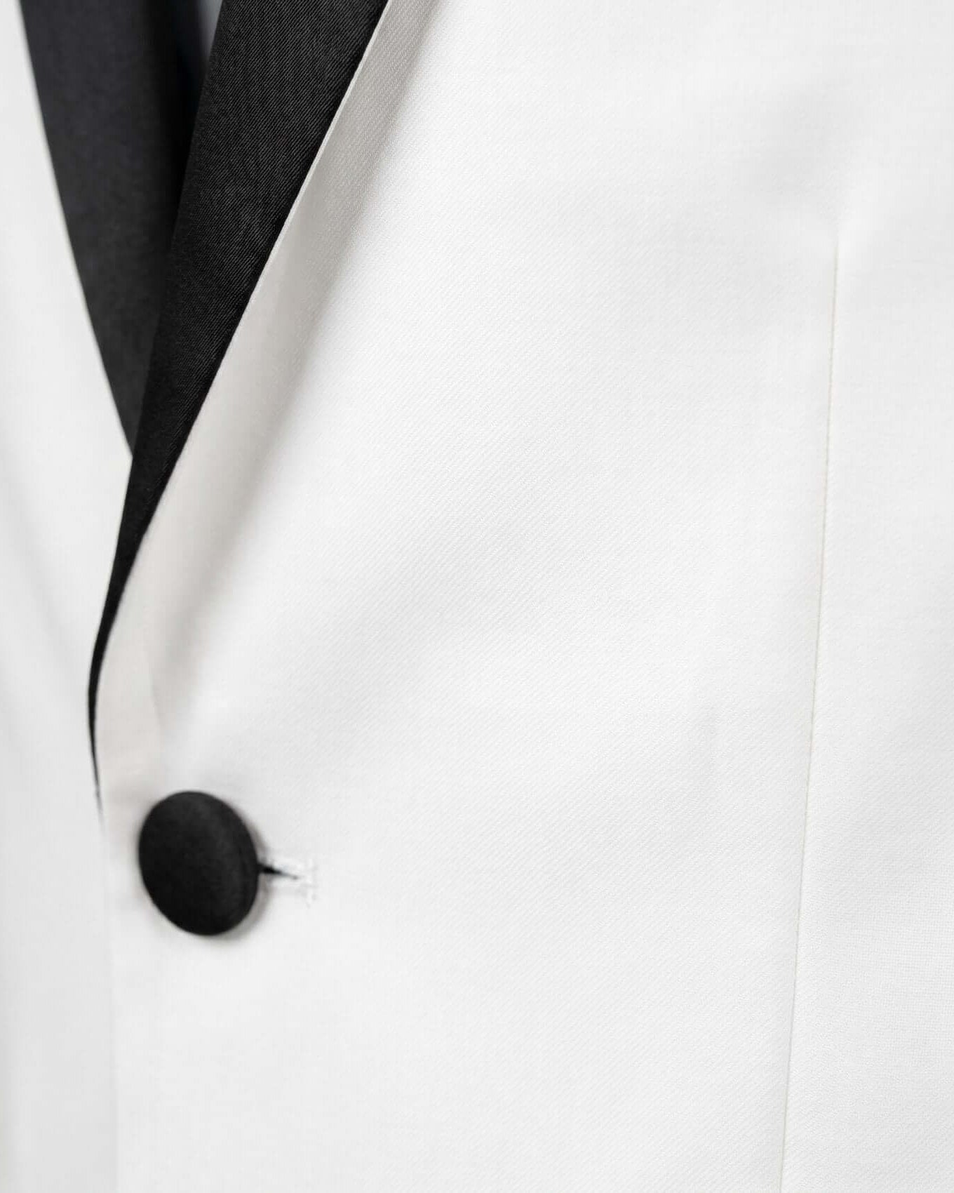 Close-up of a white suit jacket with a black lapel and button.