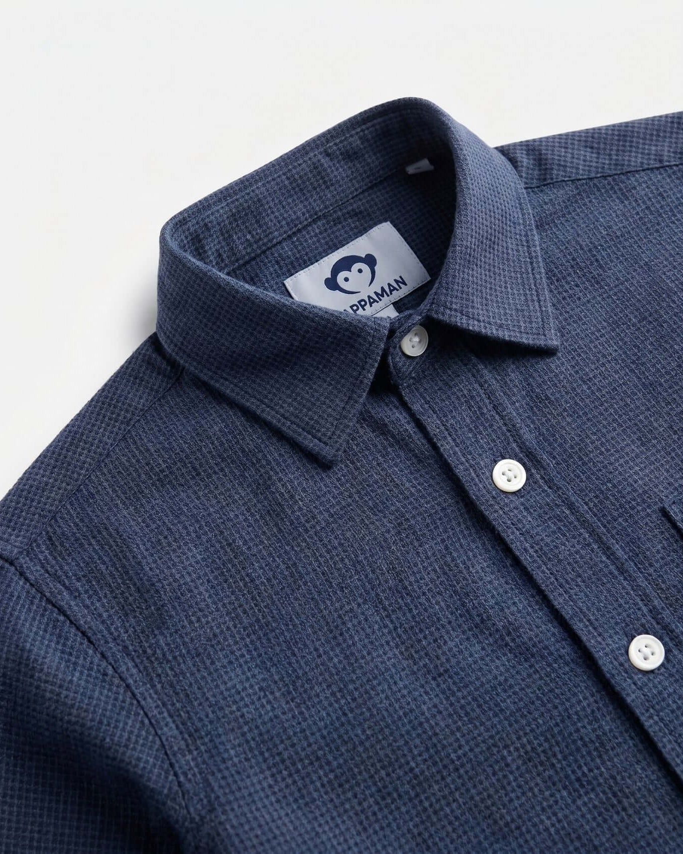Close-up of a blue textured shirt with a collar and Praman label on a light gray background