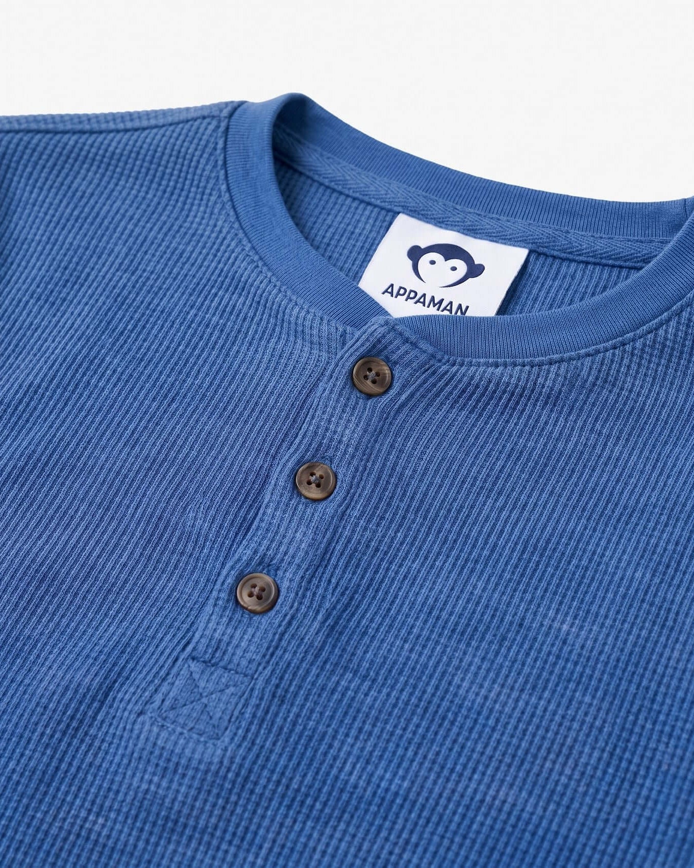 Close-up of a blue ribbed shirt with brown buttons and Appaman label.