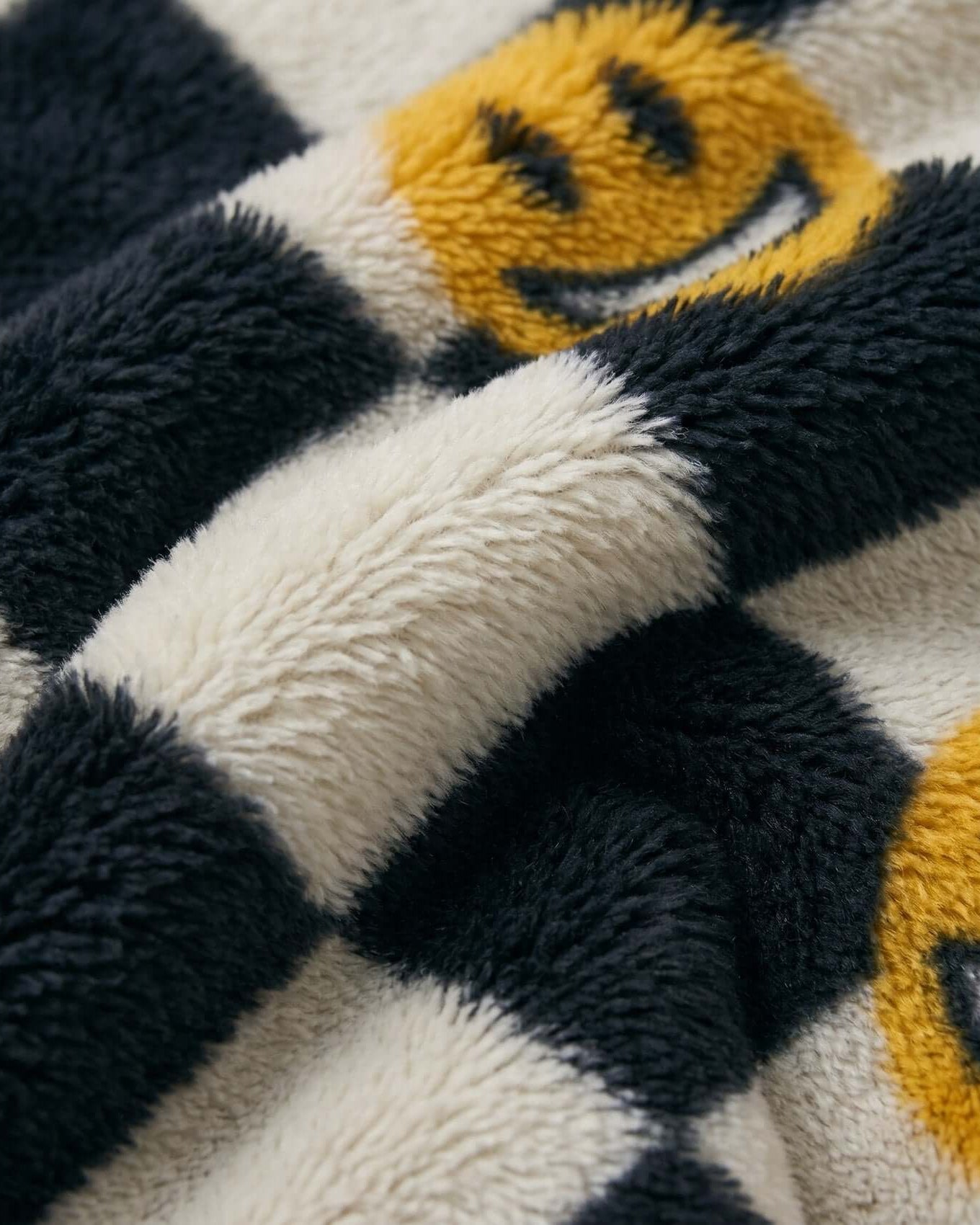 Close-up of a textured fabric with smiley face patterns in black, white, and yellow.