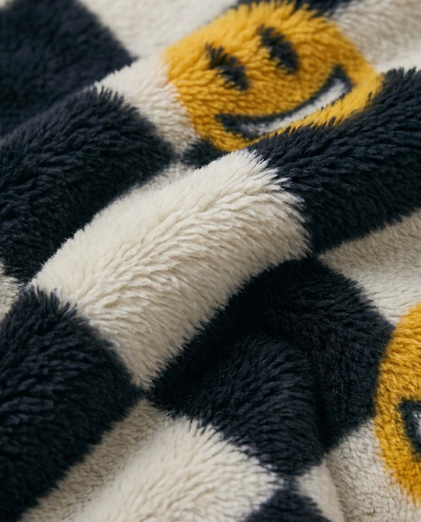 Close-up of a textured fabric with smiley face patterns in black, white, and yellow.