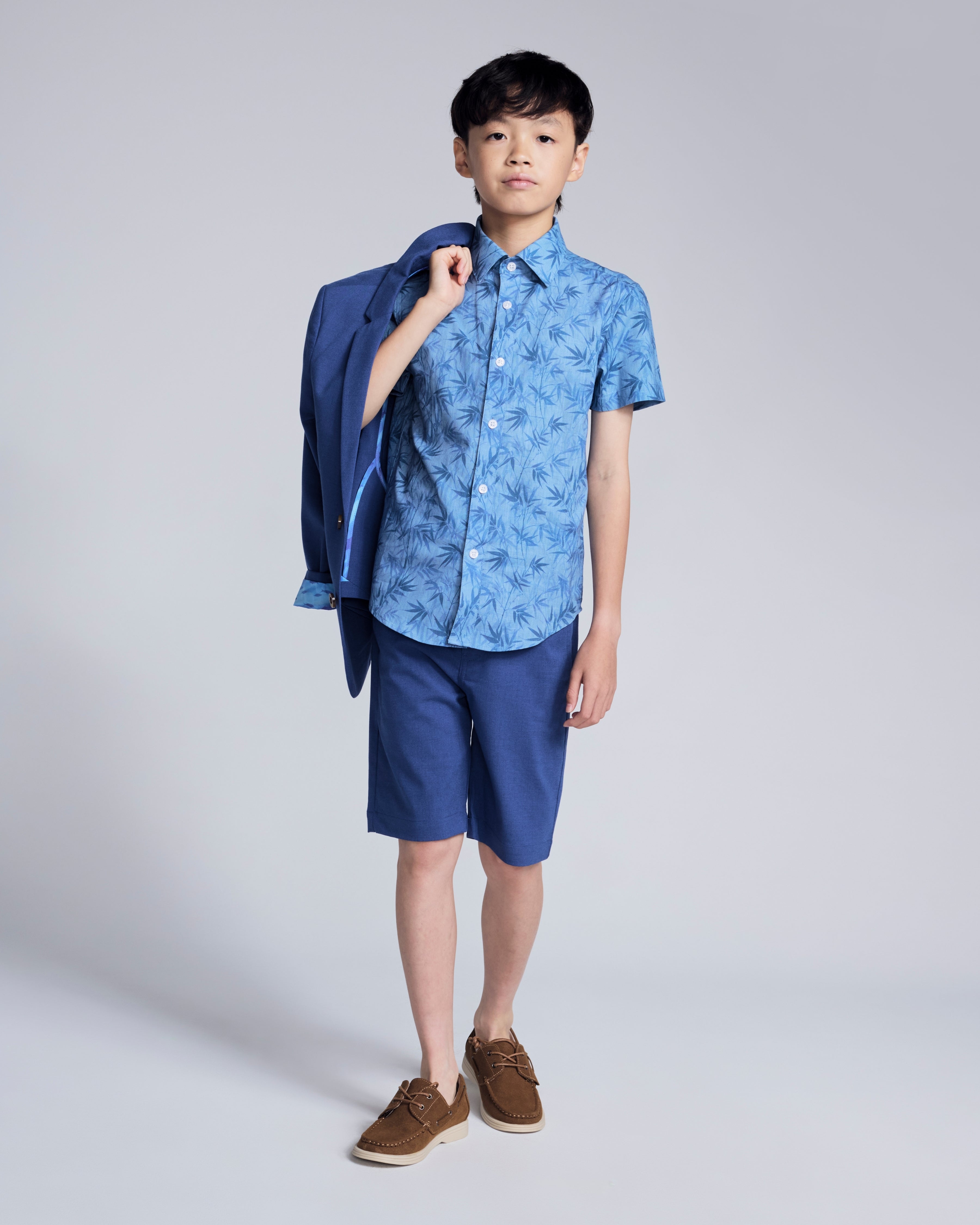 Blue Bamboo Day Party Shirt worn by a boy, features short sleeves and a spread collar, styled with shorts.