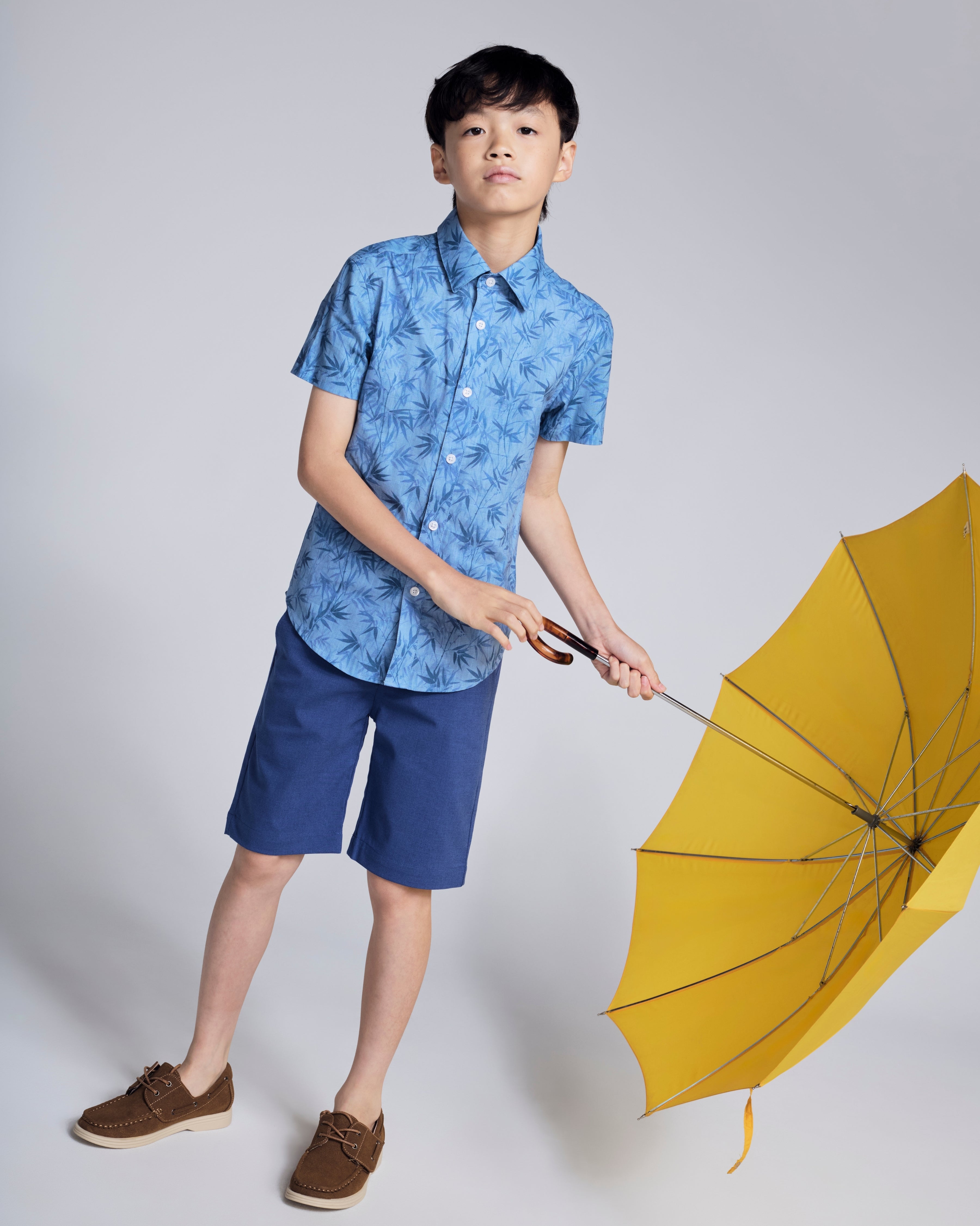 Boy wearing Blue Bamboo Day Party Shirt with yellow umbrella, perfect for warm-weather celebrations.